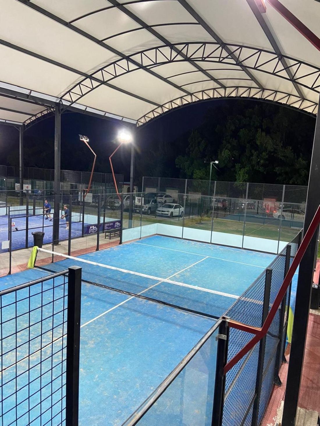 Cancha de pádel azul bajo techo con jugadores en la cancha de al lado